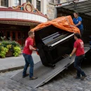 3 guys moving a piano out of a truck
